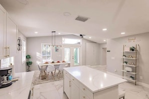 A modern kitchen with white cabinetry, a large island, and a dining area with chairs and a table. - Spacious home private heated pool, fireplace, & two kitchens-near downtown (Naples)