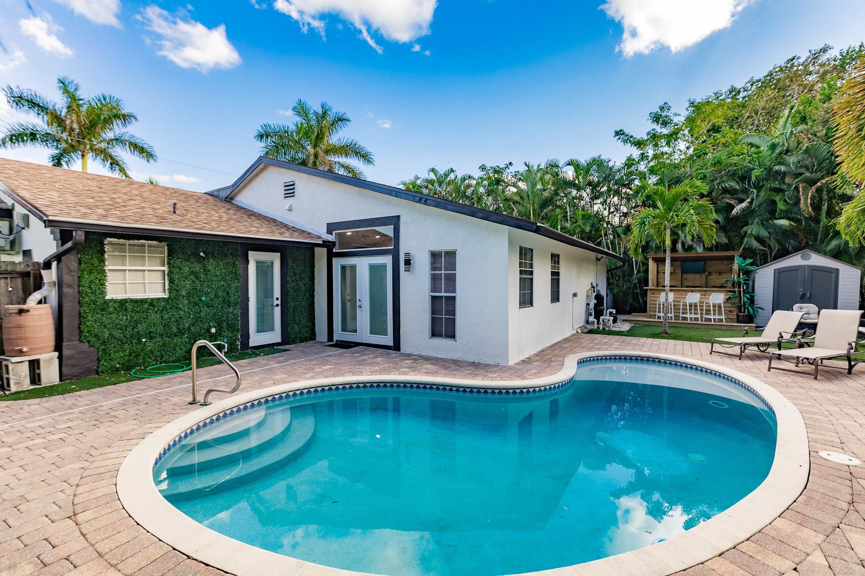 Une maison moderne dotée d’une piscine, d’une terrasse avec des chaises et d’une petite plateforme en bois.