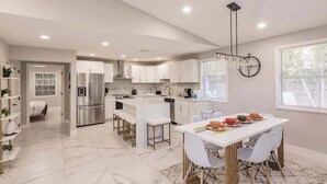 A modern kitchen with white cabinetry, a central island, and a dining area with white chairs. - Spacious home private heated pool, fireplace, & two kitchens-near downtown (Naples)