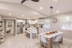 A modern kitchen with white cabinetry, a central island, and a dining area with white chairs. - Spacious home private heated pool, fireplace, & two kitchens-near downtown (Naples)