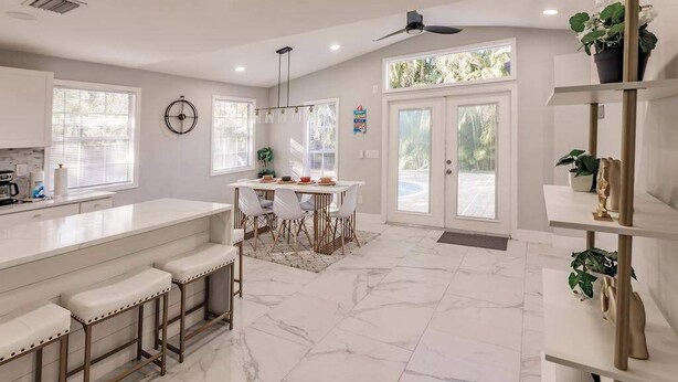 A modern kitchen with a marble floor, white cabinetry, a bar area, and a dining table with chairs. - Spacious home private heated pool, fireplace, & two kitchens-near downtown (Naples)
