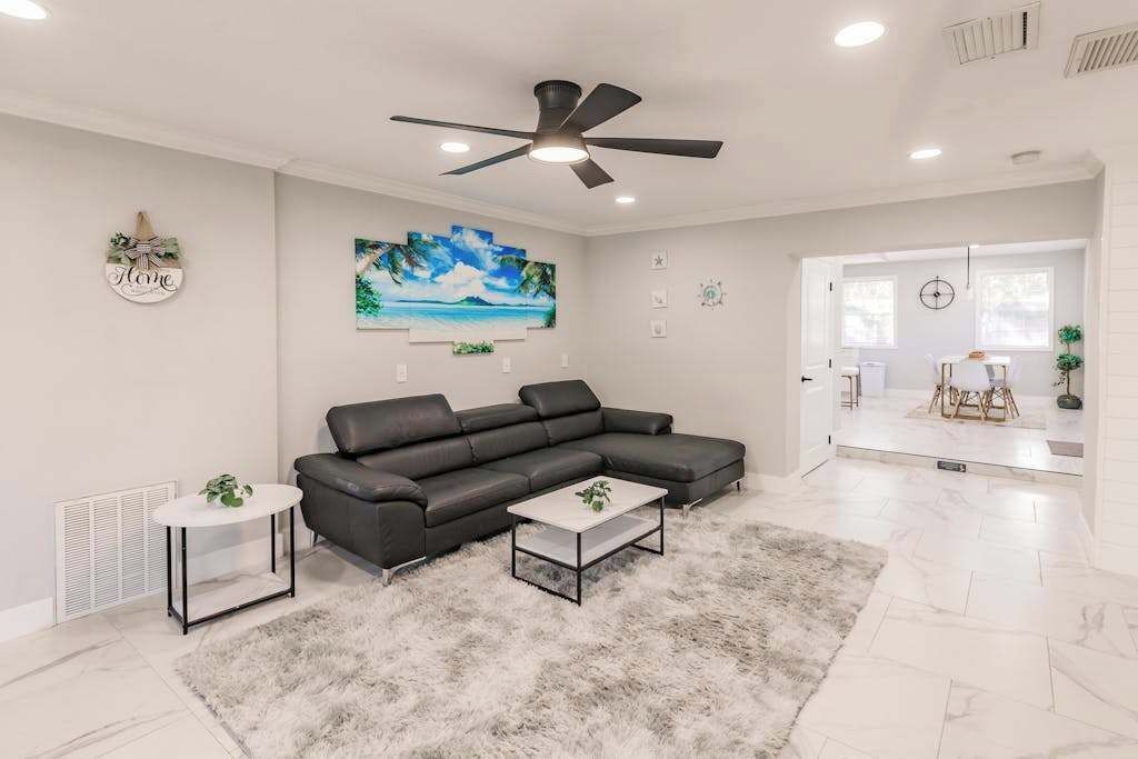 A modern living room with a sectional sofa, a coffee table, a painting, and a ceiling fan.