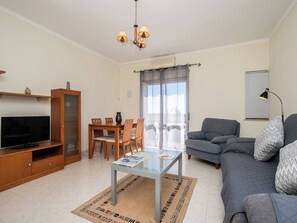 Ein Wohnzimmer mit Fernseher, einer Couch, einem Esstisch und Stühlen.