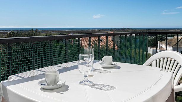 Une table ronde recouverte d’une nappe blanche, deux tasses blanches et un verre, le tout placé sur un balcon offrant une vue panoramique.