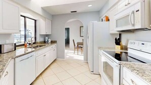 A modern kitchen with white cabinets, a granite countertop, a built-in microwave, and a refrigerator. - Snowbird Friendly Waterfront Escape with Private Pool, Dock & Serene Canal Views (Port Charlotte)