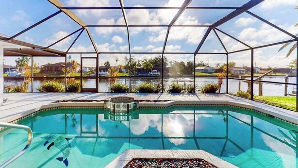 A swimming pool with a glass enclosure, surrounded by a landscaped area with plants and a view of a body of water. - Snowbird Friendly Waterfront Escape with Private Pool, Dock & Serene Canal Views (Port Charlotte)