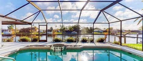 A swimming pool with a glass enclosure, surrounded by a landscaped area with plants and a view of a body of water.