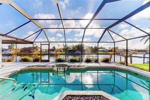 Una piscina con cerramiento de vidrio, rodeada de jardines y vistas a una masa de agua.