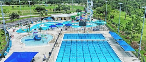 A large swimming pool with multiple lanes, a water slide, and a separate pool area with lounge chairs and umbrellas.