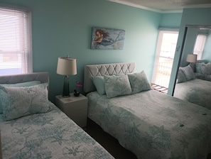 A bedroom with two beds, a nightstand with a lamp, a painting on the wall, and a window with blinds. - beyond paradise a lovely 2 bedroom 2 bath condo (Nags Head)