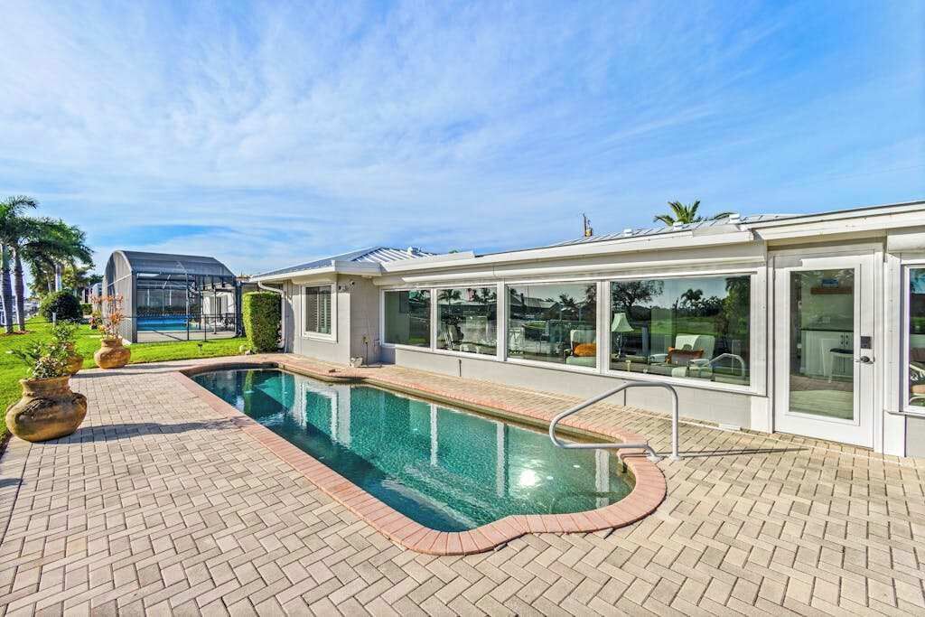 A swimming pool with a brick deck, glass enclosure, and a covered area with seating.