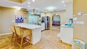 Una cocina moderna con una isla central, taburetes de bar, un refrigerador y una zona de comedor con sofá.