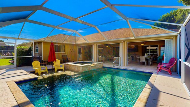 Una piscina con cerramiento de vidrio, sillas amarillas y un jacuzzi.