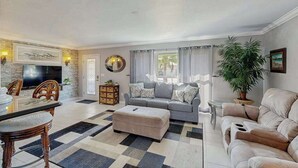 Un salon avec un canapé, un pouf et un téléviseur. On y trouve également une table à manger avec des chaises.