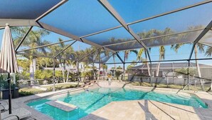 Une piscine entourée d’une structure en verre, avec des chaises longues et des palmiers tout autour.