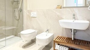 Un baño moderno con cabina de ducha de vidrio, un lavabo blanco y un mueble de tocador de madera.