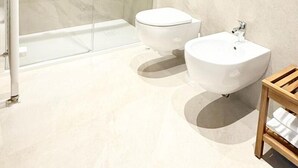 Un baño moderno con ducha de vidrio, dos inodoros, un lavamanos y una mesita de madera.