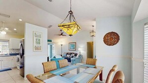 A dining area with a glass-top table, wicker chairs, a hanging pendant light, and a wall-mounted decorative piece. - Dog-friendly home w/private salt water in ground pool & close to Shamrock Park (Venice)