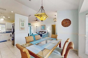 A dining area with a glass-top table, wicker chairs, a hanging pendant light, and a wall-mounted decorative piece. - Dog-friendly home w/private salt water in ground pool & close to Shamrock Park (Venice)