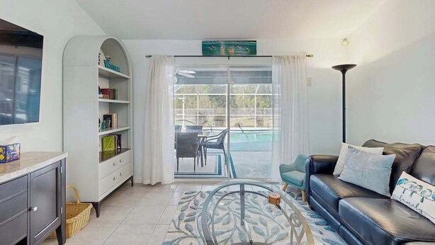 A living room with a sofa, a coffee table, a bookshelf, and a view of a pool through a glass door. - Dog-friendly home w/private salt water in ground pool & close to Shamrock Park (Venice)