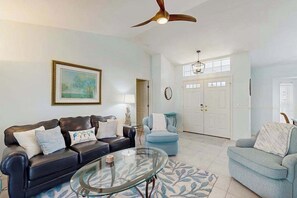 A living room with a black leather sofa, a blue armchair, a glass coffee table, a ceiling fan, and a framed picture on the wall. - Dog-friendly home w/private salt water in ground pool & close to Shamrock Park (Venice)