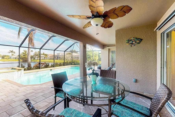 Ein Tisch mit Glasplatte, Stühle, Deckenventilator und Blick auf einen Swimmingpool.