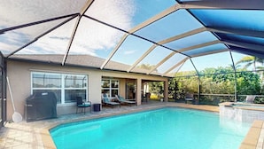A swimming pool with a covered patio area, a grill, and outdoor furniture. - Beautiful Lakefront Home with Private Pool/Spa, Furnished Lanai, Grill, & WiFi (Fort Myers)