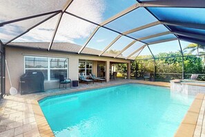 Ein Schwimmbad mit überdachtem Patio, Grill und Gartenmöbeln.