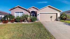 A residential house with a garage, a well-maintained lawn, and various shrubs. - Beautiful Lakefront Home with Private Pool/Spa, Furnished Lanai, Grill, & WiFi (Fort Myers)