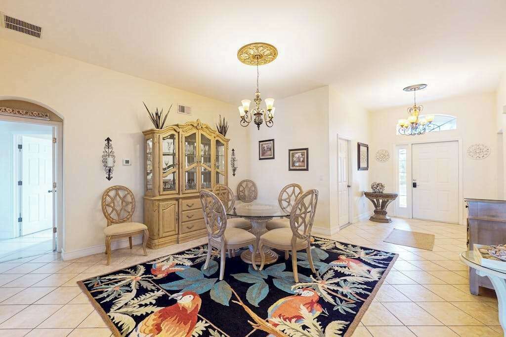 A dining area with a round table, chairs, a chandelier, a cabinet, and a patterned rug.