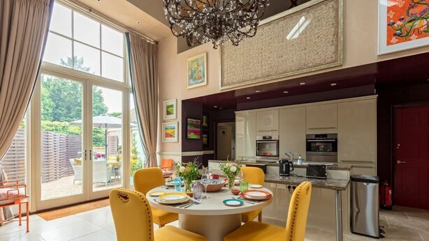 Ein Essbereich mit einem runden Tisch, gelben Stühlen und Blick auf den Garten durch große Fenster.