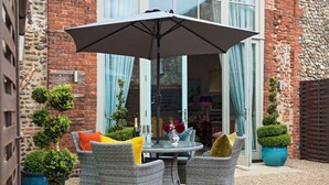 Eine Terrasse mit Korbstühlen, einem Tisch und einem großen Sonnenschirm.