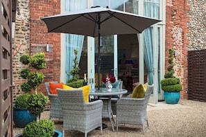 Eine Terrasse mit Korbstühlen, einem Tisch und einem großen Sonnenschirm.