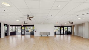 A spacious room with a wooden floor, ceiling fans, and large windows. - Beachfront condo with balcony, community pool, and Wifi (Fort Myers Beach)