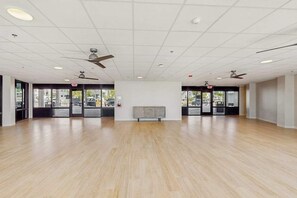 A spacious room with a wooden floor, ceiling fans, and large windows. - Beachfront condo with balcony, community pool, and Wifi (Fort Myers Beach)