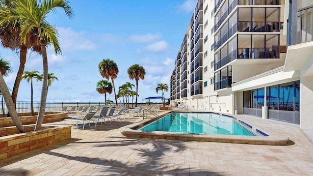A pool area with lounge chairs, palm trees, and a building with balconies. - Beachfront condo with balcony, community pool, and Wifi (Fort Myers Beach)