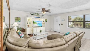 Ein Wohnzimmer mit beiger Couch, Couchtisch, Fernseher und Deckenventilator.