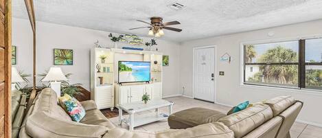 Una sala de estar con un sofá color beige, una mesa de centro, un televisor y un ventilador de techo.