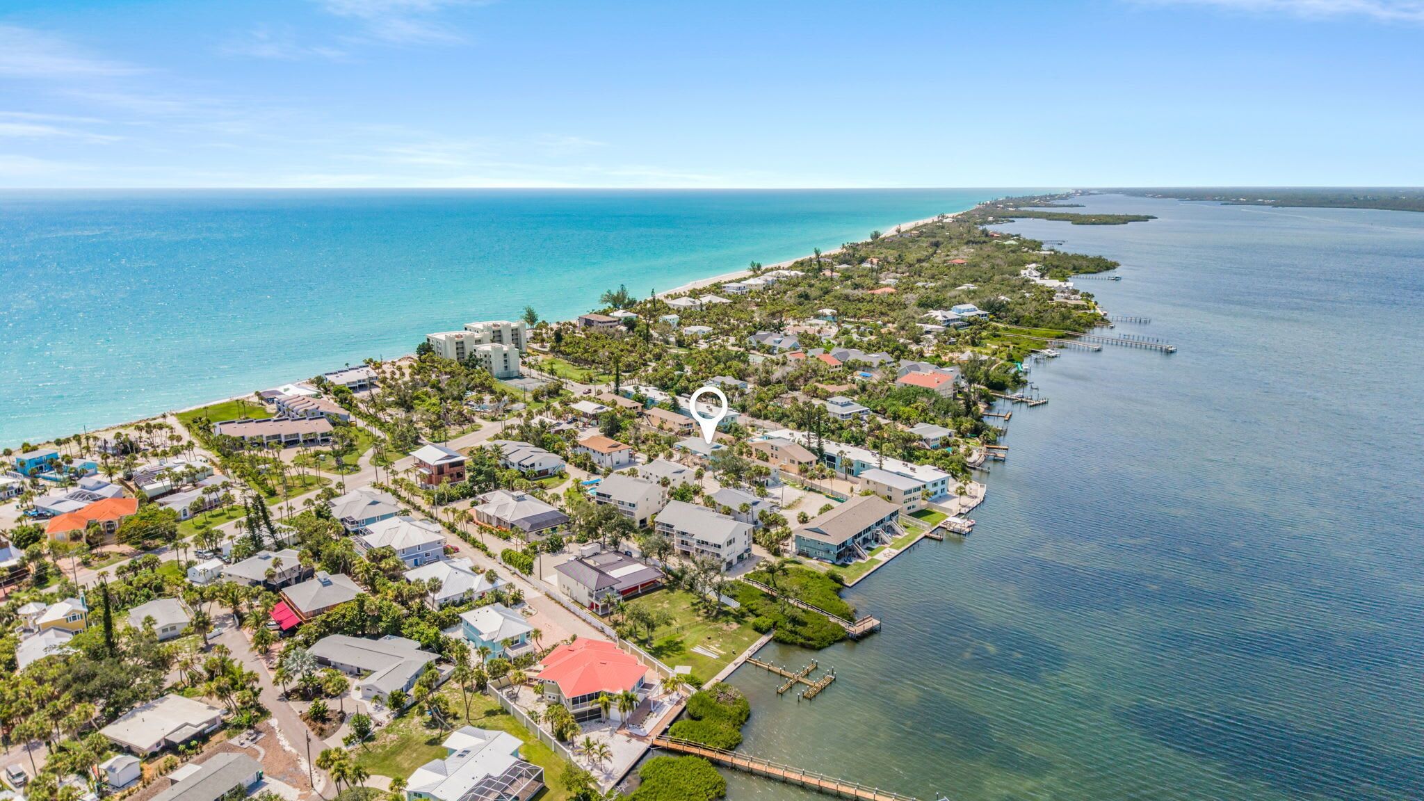 An aerial view of a coastal residential area with houses, a marina, and a beach.