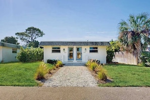 A single-story house with a front entrance, a gravel driveway, and a wooden fence.