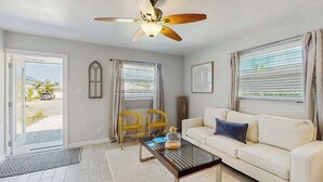 A living room with a ceiling fan, a white sofa, two yellow chairs, and a coffee table. - Spacious master duplex w full kitchen, close to beach & shopping (Naples)