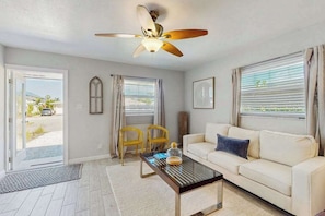 A living room with a ceiling fan, a white sofa, two yellow chairs, and a coffee table.