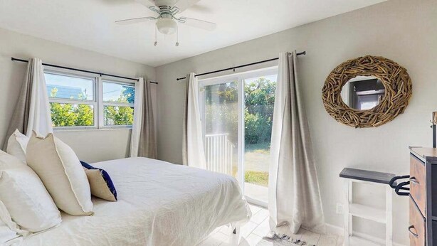 A bedroom with a bed, a ceiling fan, a window with curtains, a door leading to a balcony, and a dresser. - Spacious master duplex w full kitchen, close to beach & shopping (Naples)