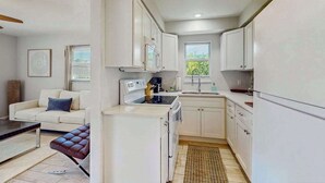 A compact kitchen with white cabinets, a stove, and a sink. There is a brown leather bench and a white sofa in the adjacent living area. - Spacious master duplex w full kitchen, close to beach & shopping (Naples)
