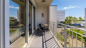 A balcony with a glass door, two chairs, a small table, and a view of buildings and greenery. - Talea Sun Sea Haven 1BR Apartment (Shënkoll)