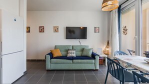 A living room with a sofa, a flat-screen TV, and a dining area with a table and chairs. - Talea Sun Sea Haven 1BR Apartment (Shënkoll)