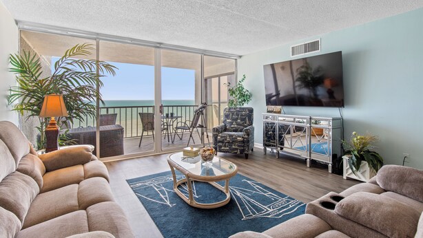 Ein Wohnzimmer mit Sofa, Couchtisch, Fernseher und einem Balkon mit Blick.