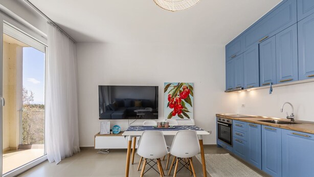 Una cocina moderna con armarios azules, una mesa de comedor con sillas, un televisor de pantalla plana y un ventanal con cortinas.