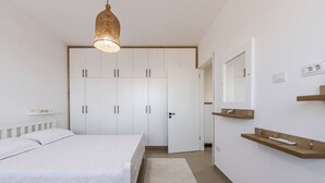 Un dormitorio con cama, armario, mesita de noche, espejo y lámpara colgante.