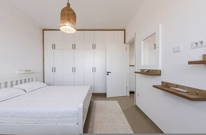 Een slaapkamer met een bed, kledingkast, nachtkastje, spiegel en een hanglamp.